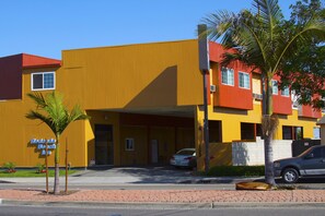 A yellow building with a red roof, a palm tree, and a car parked in front.