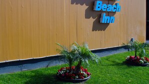 A sign for Redondo Beach Inn with a wooden facade and two flower beds in front. - Redondo Beach Inn (Gardena)