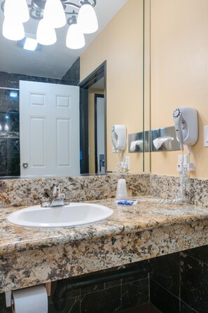 A bathroom with a granite countertop, a white sink, a mirror, and two hair dryers mounted on the wall.