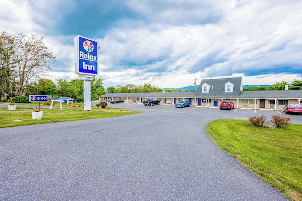 A motel with a signboard, parking area, and a building with multiple rooms.
