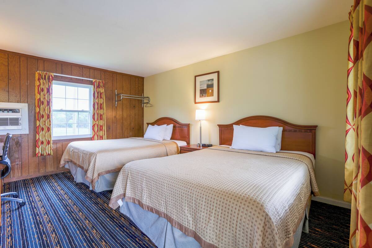 A hotel room with two beds, a desk, and a window with curtains.