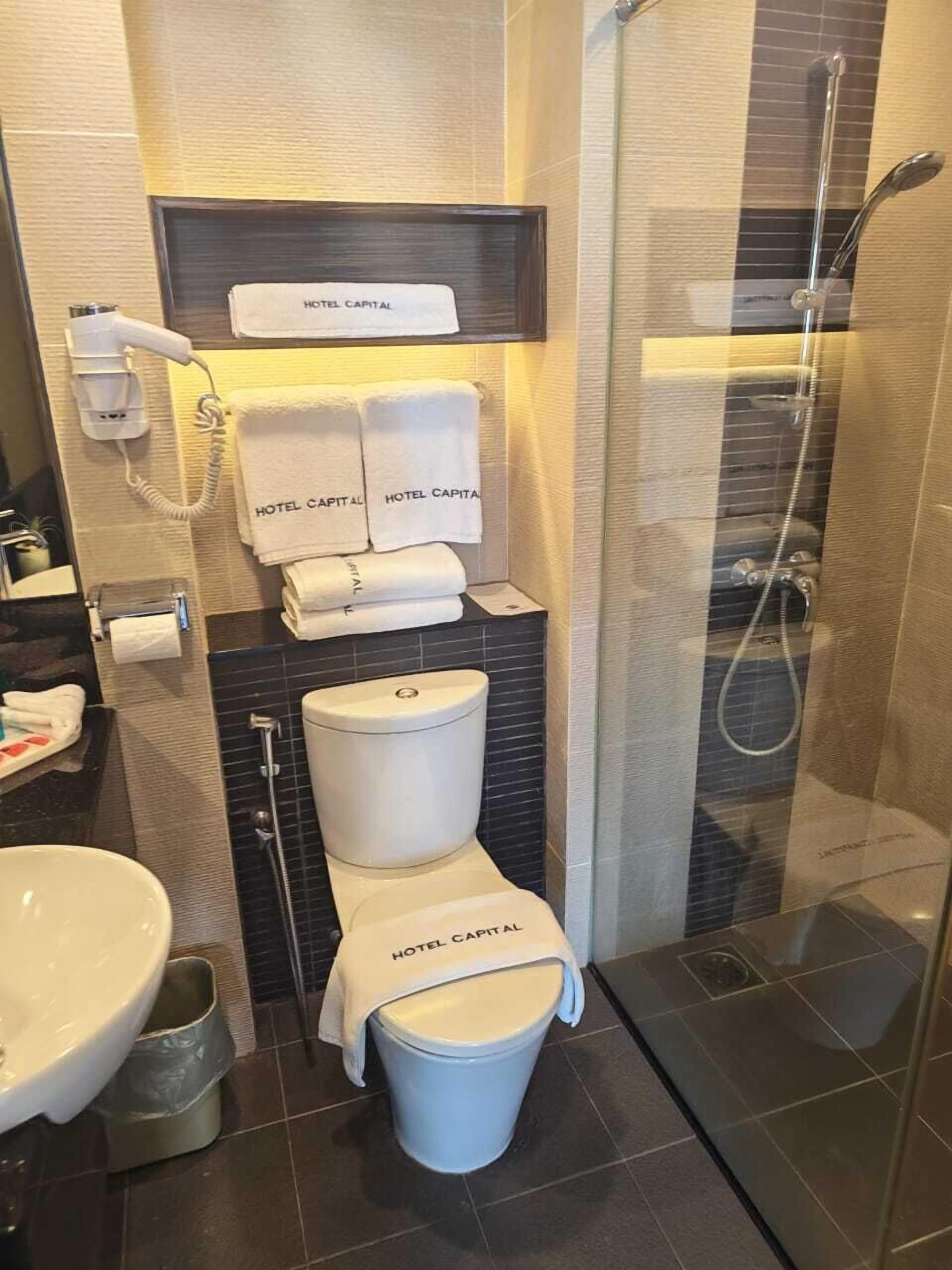 A modern bathroom with a toilet, bidet, and shower. There are towels and a hairdryer on the wall.