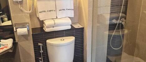 A modern bathroom with a toilet, bidet, and shower. There are towels and a hairdryer on the wall.