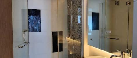 Un baño moderno con ducha envuelta en vidrio, bañera independiente y un espejo grande.