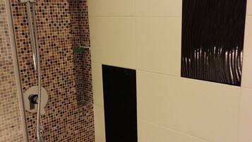 A shower area with a glass door, tiled walls, and a black rectangular object on the wall.