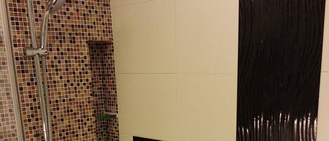 A shower area with a glass door, tiled walls, and a black rectangular object on the wall.