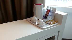 Hotelkamer met een wit bureau, een koffiezetapparaat, een waterfles en een dienblad met bekers en een zakje snacks.