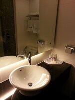 Ein Badezimmer mit einem großen weißen Waschbecken, einem Spiegel, einer Dusche und einem Handtuchhalter mit Handtüchern.