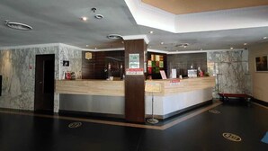 Een hotel receptie met marmeren wanden, een receptiebalie en een digitaal informatiebord.