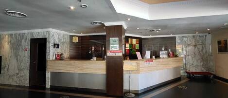 A hotel reception area with marble walls, a reception desk, and a digital information board.