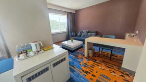 Een hotelkamer met een bank, een salontafel, een kleine eettafel, een kitchenette en een groot raam.