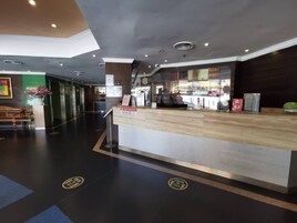 Un área de recepción de hotel con diseño moderno, que incluye un mostrador de recepción, un espacio de descanso y vistas a la calle a través del ventanal.