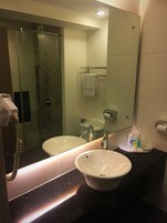 A bathroom with two sinks, a glass shower enclosure, a towel rack, and a mirror reflecting the room.