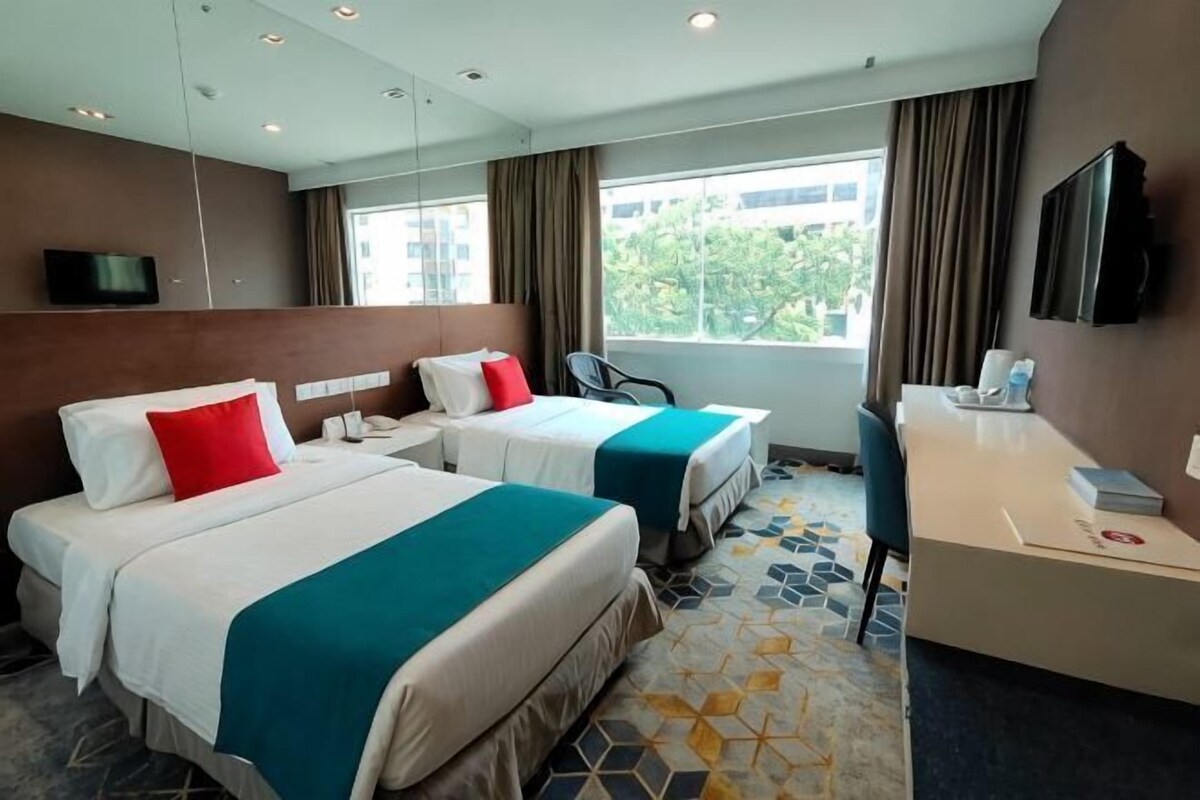 A hotel room with two beds, a desk, a chair, a TV, and a window with curtains.