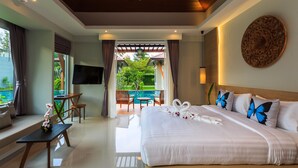 A hotel room with a large bed, a TV, a balcony with a view of a pool, and a dining area. - Khaolak Forest Resort (Takua Pa)