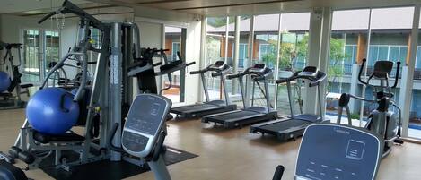 Une salle de sport moderne, dotée de divers appareils d’entraînement, de grandes fenêtres et offrant une vue sur l’extérieur.