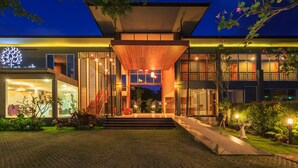A modern building with a glass facade, a wooden entrance canopy, and a well-lit outdoor area with steps leading to the entrance. - Khaolak Forest Resort (Takua Pa)