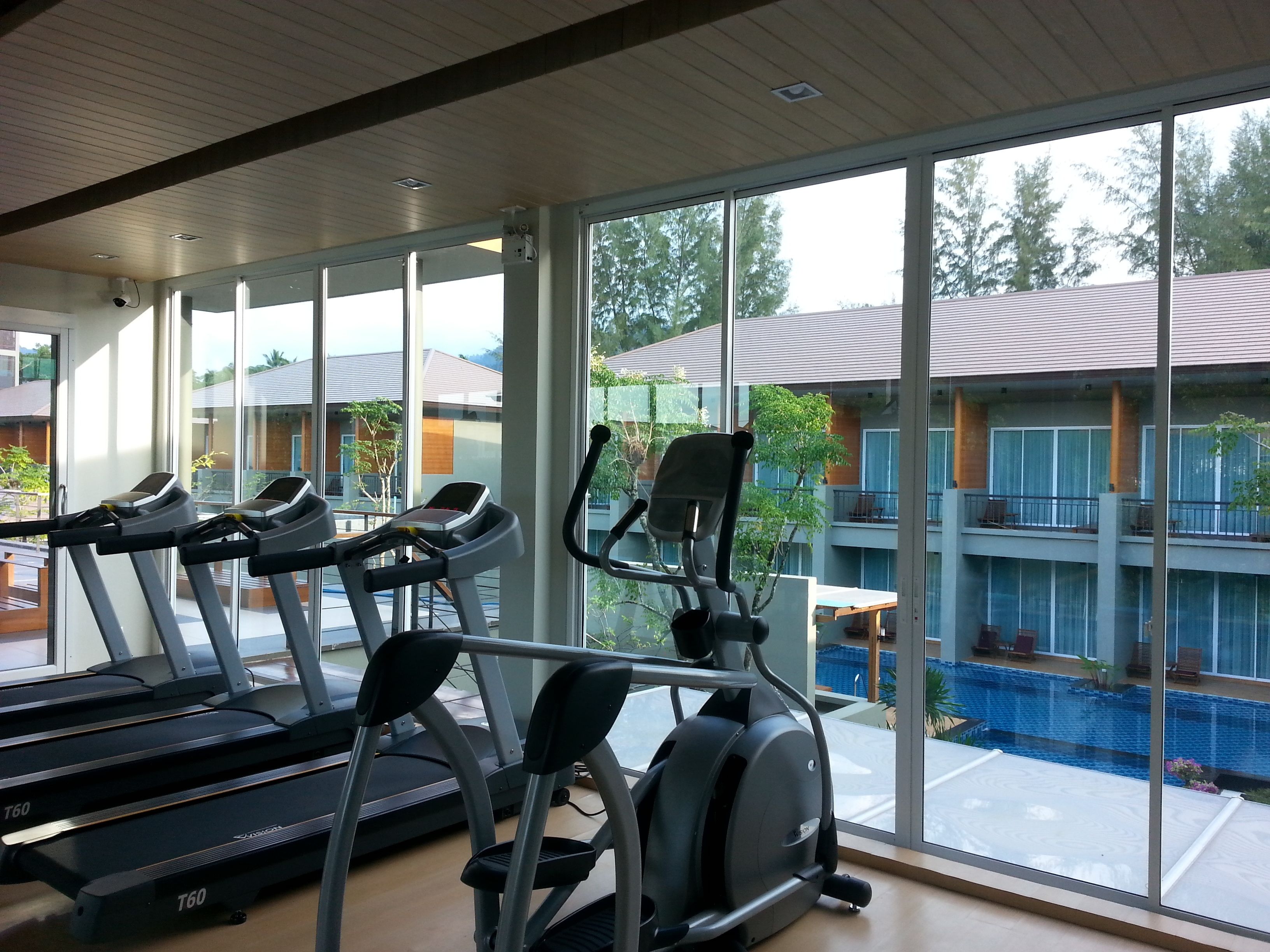A gym with treadmills and an elliptical machine, large windows, and a view of a swimming pool and buildings.