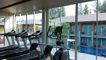 A gym with treadmills and an elliptical machine, large windows, and a view of a swimming pool and buildings.