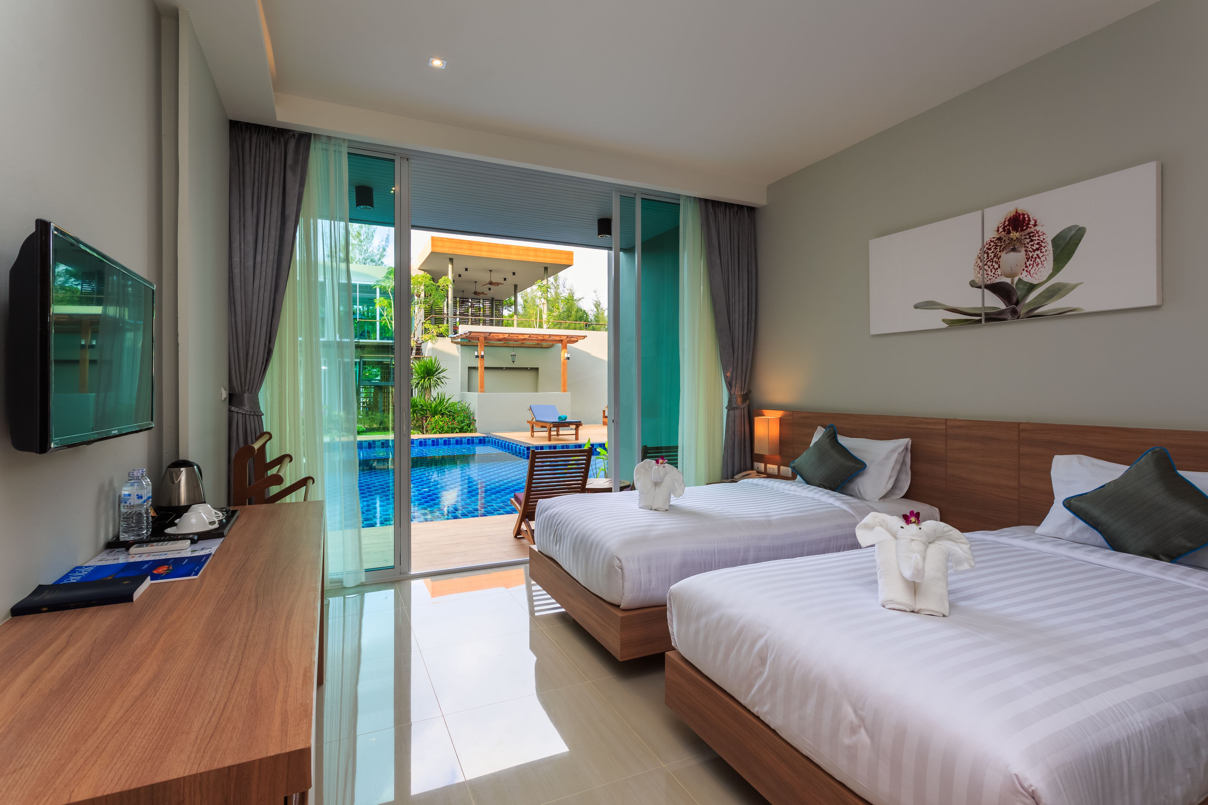 A hotel room with two beds, a desk, a TV, and a view of an outdoor swimming pool.