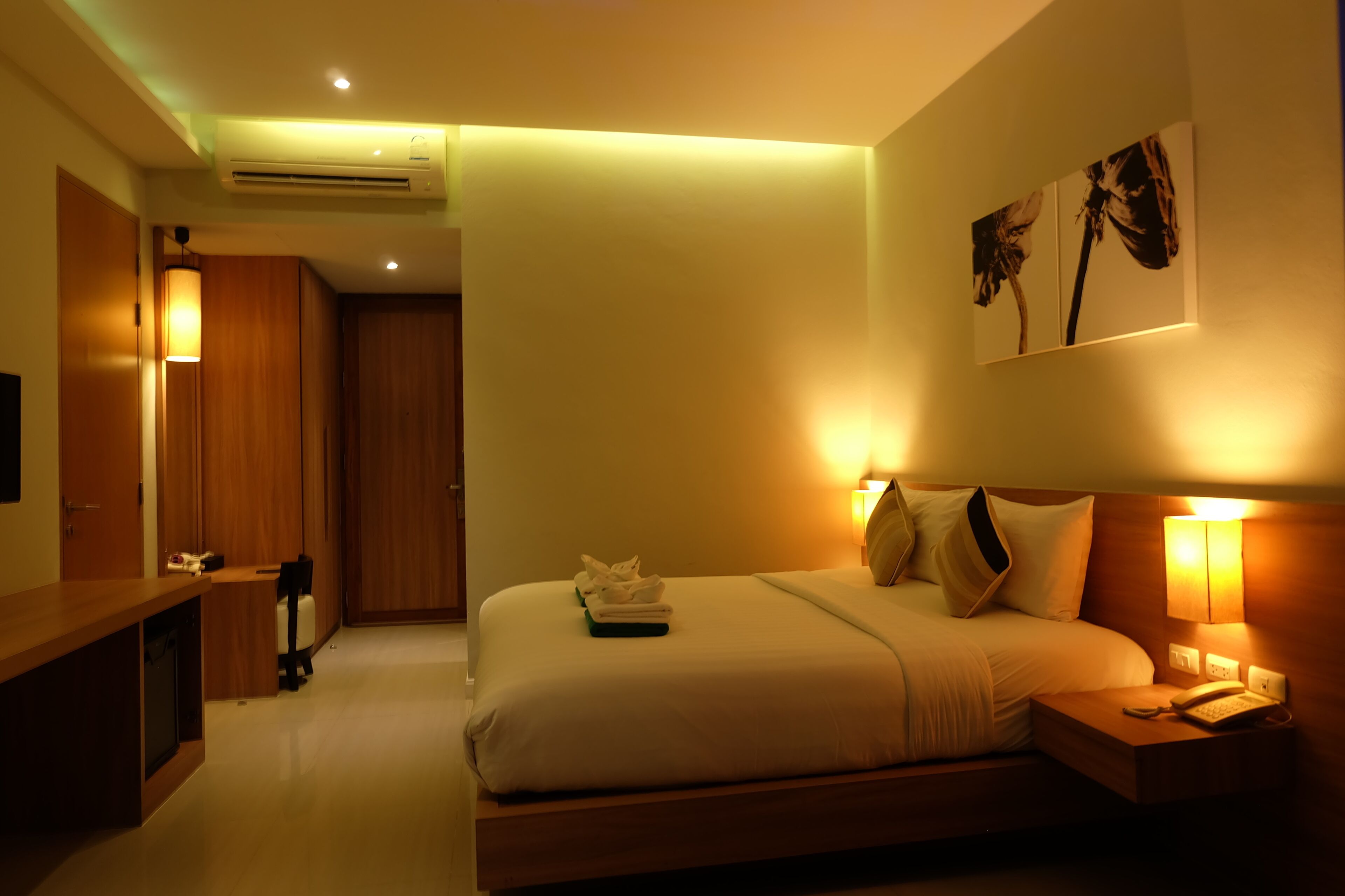 Una habitación de hotel con cama, mesita de noche, lámpara y una obra de arte en la pared.