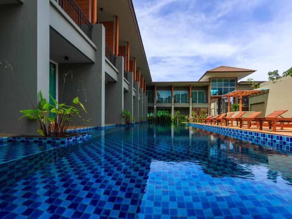 Un hotel moderno con piscina, mobiliario exterior y un cielo azul despejado.