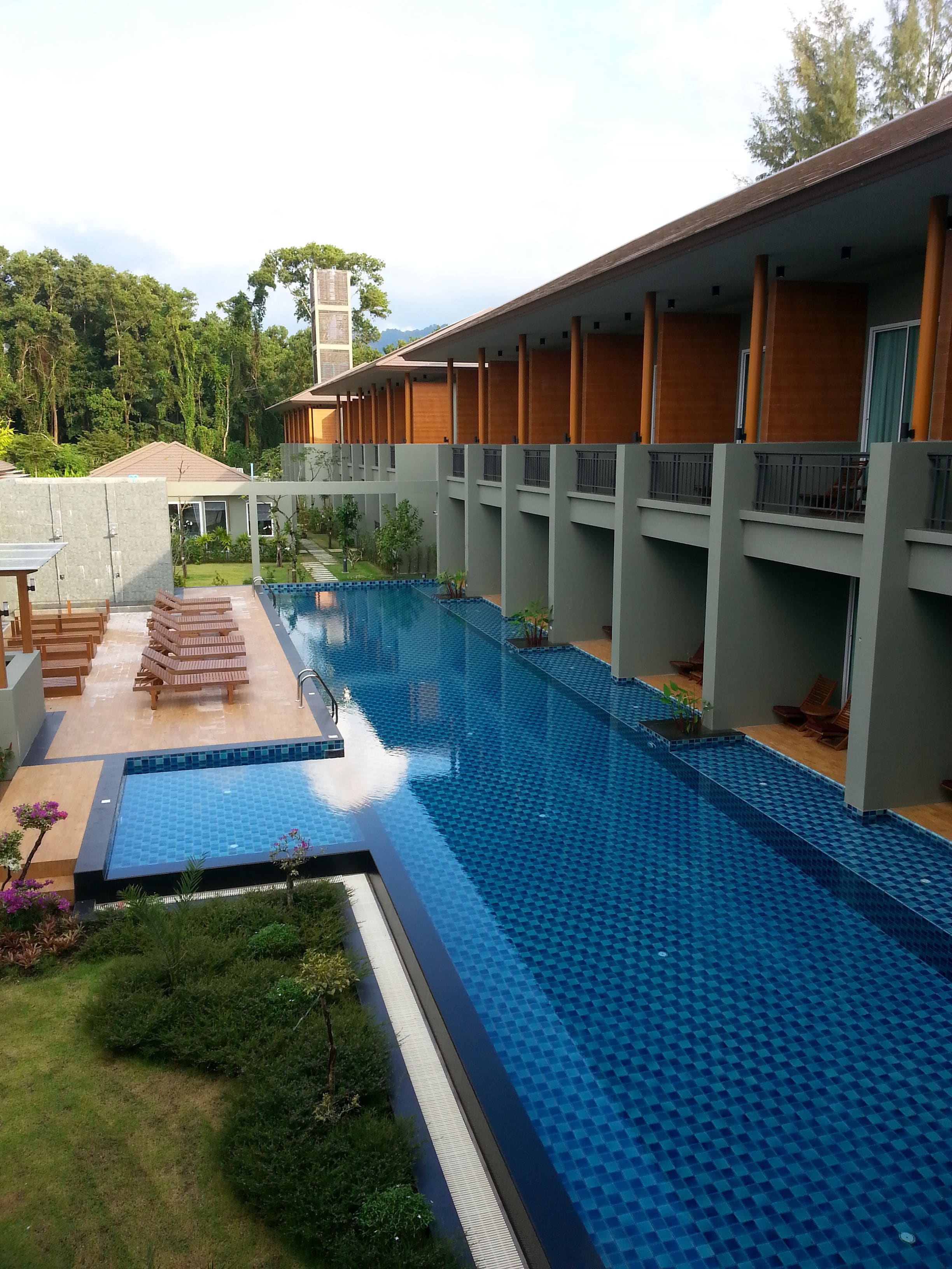 A swimming pool with a tiled deck area, surrounded by a covered walkway with wooden benches.