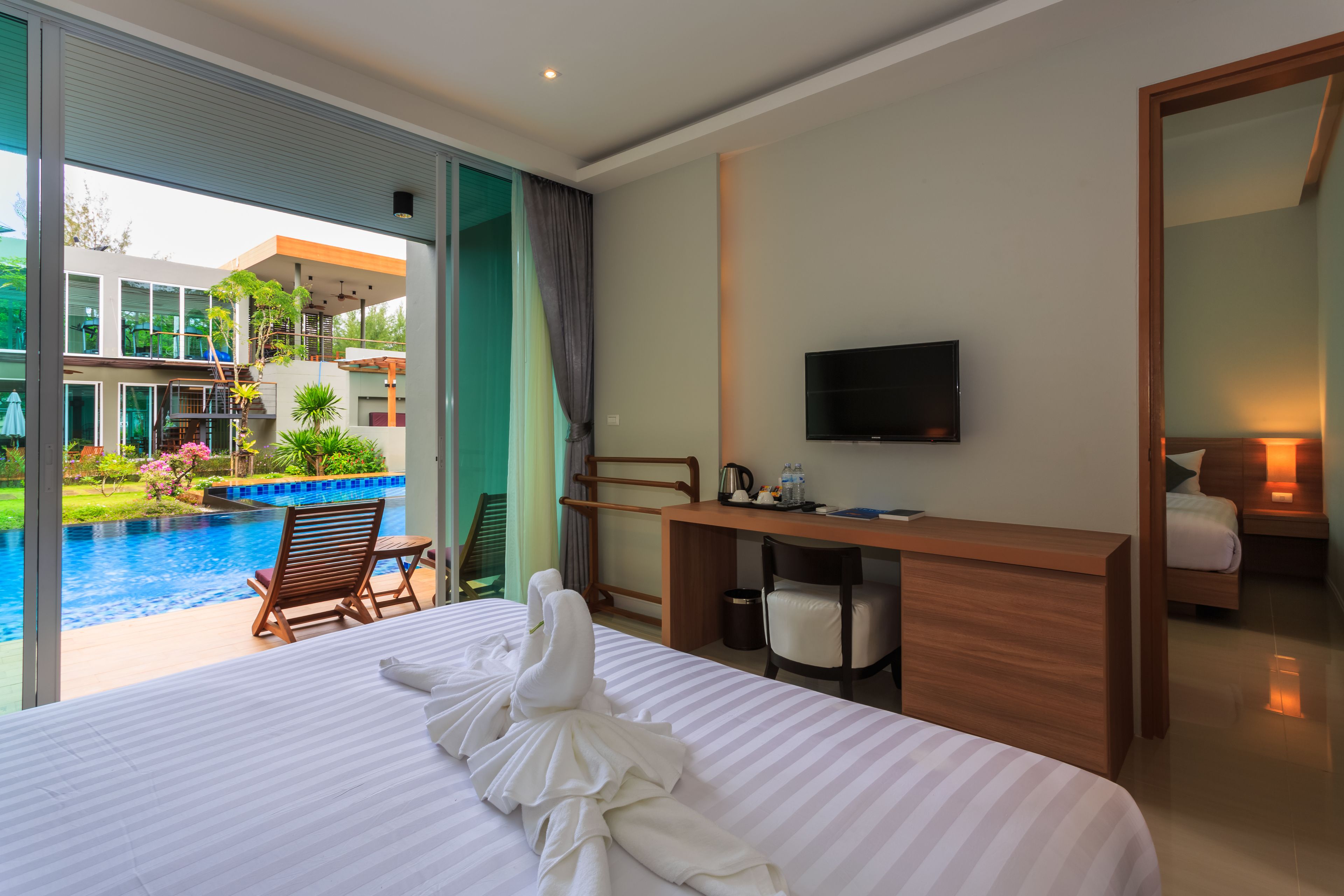 Quarto de hotel com cama grande, mesa de escritório, televisão e vista para uma piscina e um edifício.