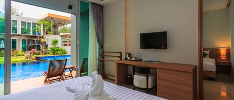 Quarto de hotel com cama grande, mesa de escritório, televisão e vista para uma piscina e um edifício.