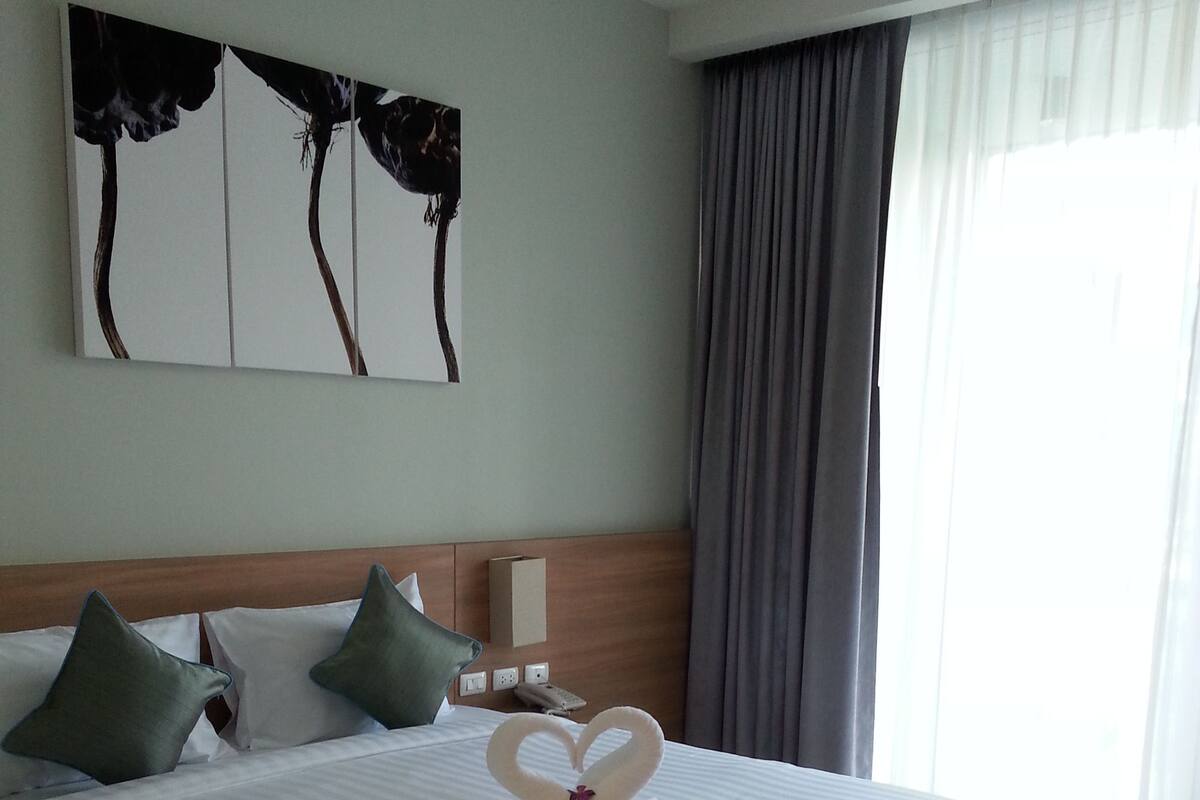 Un grand lit agrémenté d’une décoration en forme de cœur réalisée avec des serviettes, une tête de lit en bois et une œuvre d’art accrochée au mur.