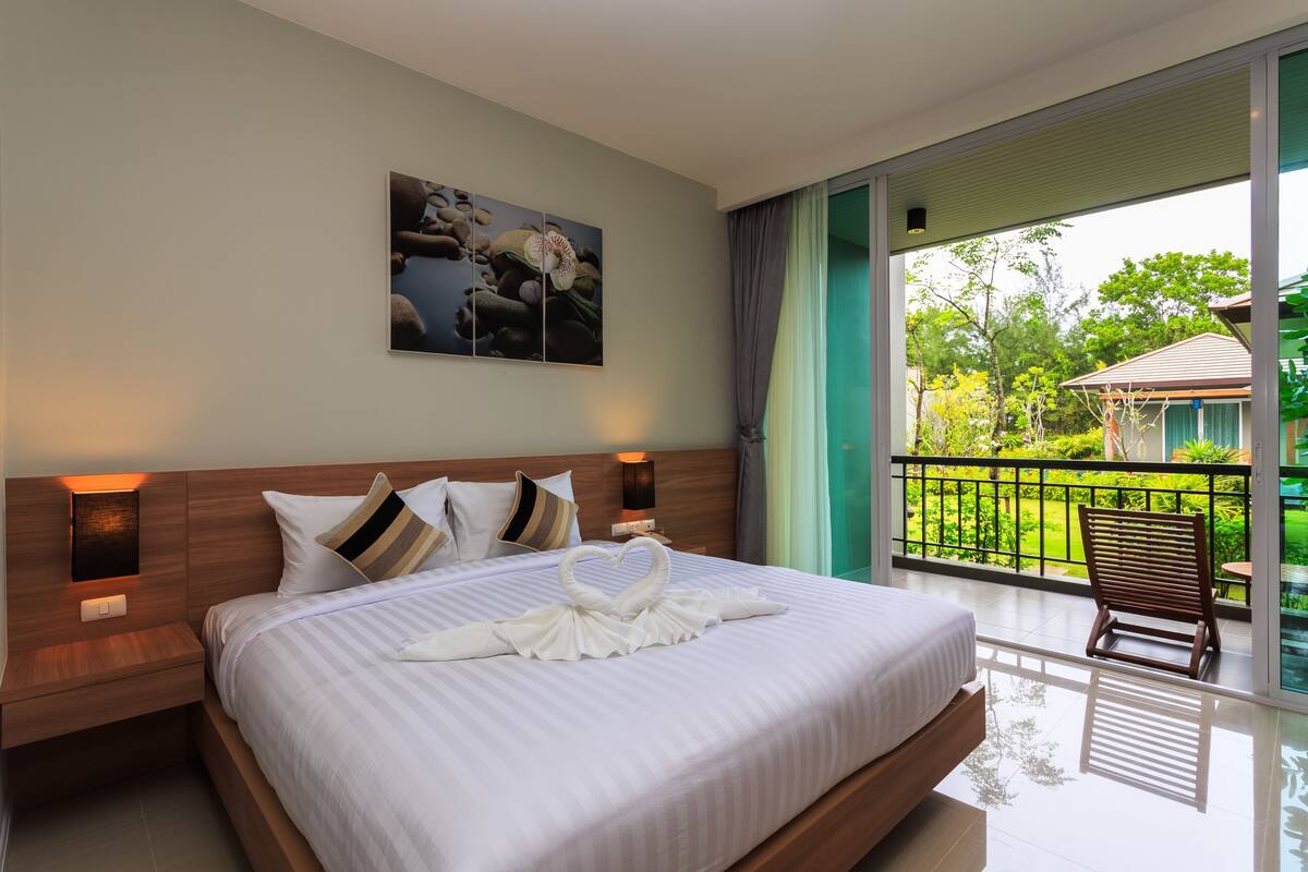 Une chambre d’hôtel avec un grand lit, une vue sur le jardin et un balcon avec une chaise.