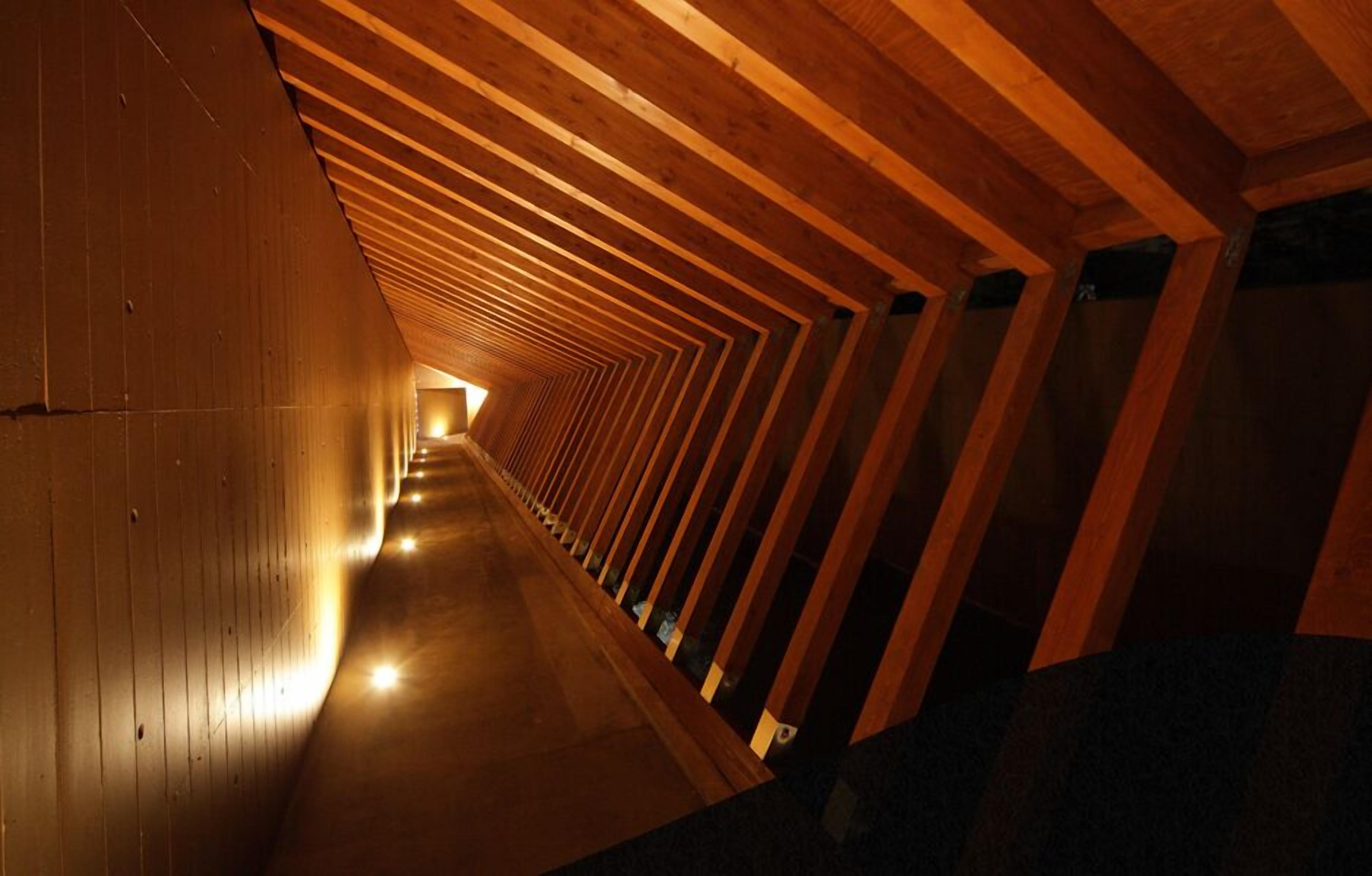 A long, narrow corridor with wooden beams on the ceiling and walls, creating a tunnel-like effect.