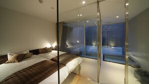 A modern bedroom with a large bed, a glass partition, and a view of a cityscape. - Four Seasons Yuzawa Quattro (Yuzawa)