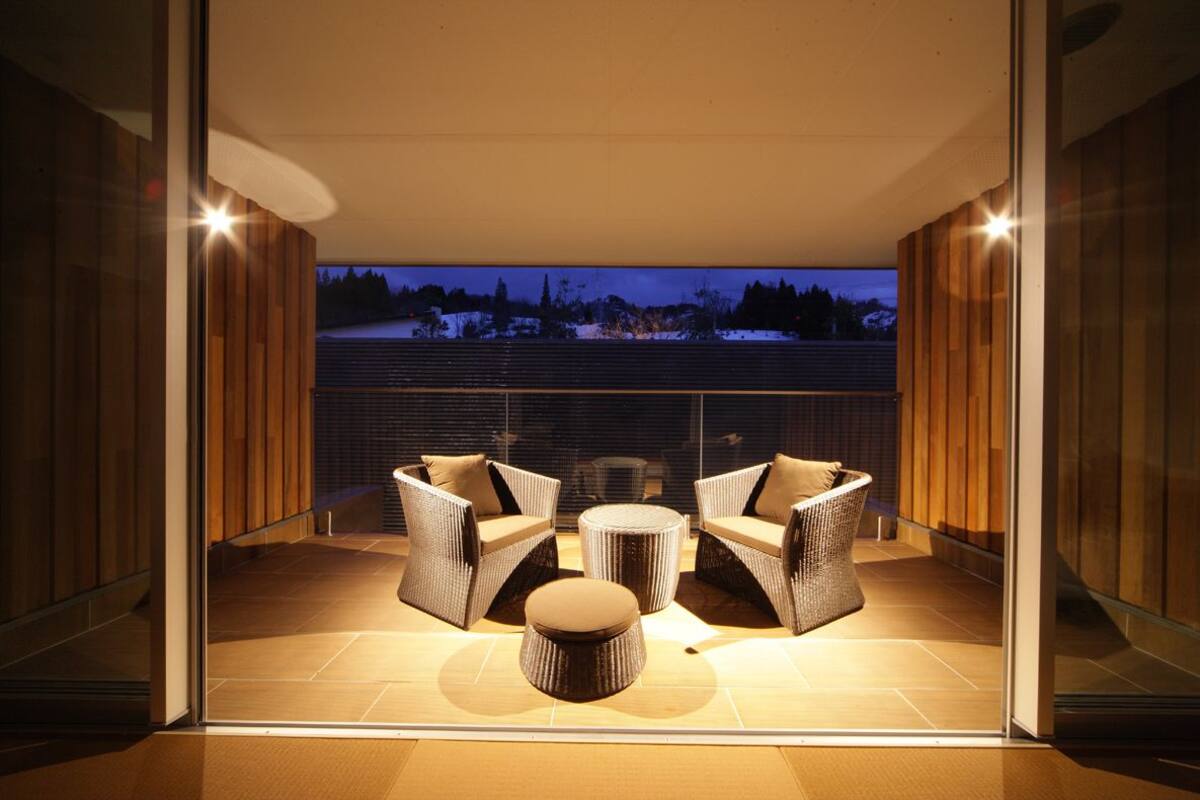 Een balkon met rieten meubels en een ronde tafel, met uitzicht op een besneeerd landschap.