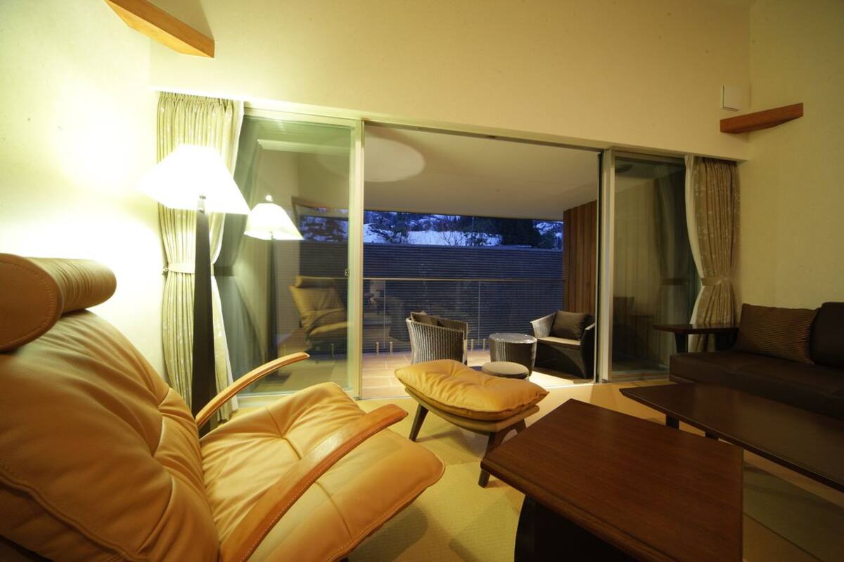 Een moderne woonkamer met lederen banken, een houten salontafel en een glazen deur die leidt naar een balkon.