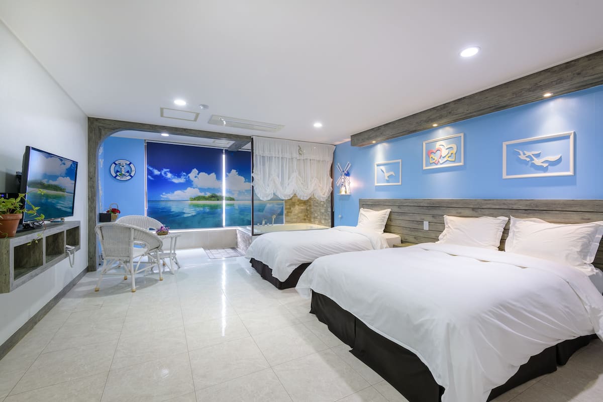 A hotel room with two beds, a desk with a chair, a large window with a view, and artwork on the walls.