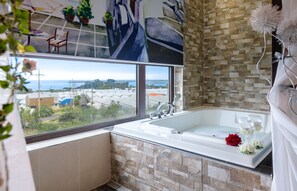 A bathroom with a large window, a bathtub, and a view of a coastal area. - Famille Spa Resort (Seogwipo)