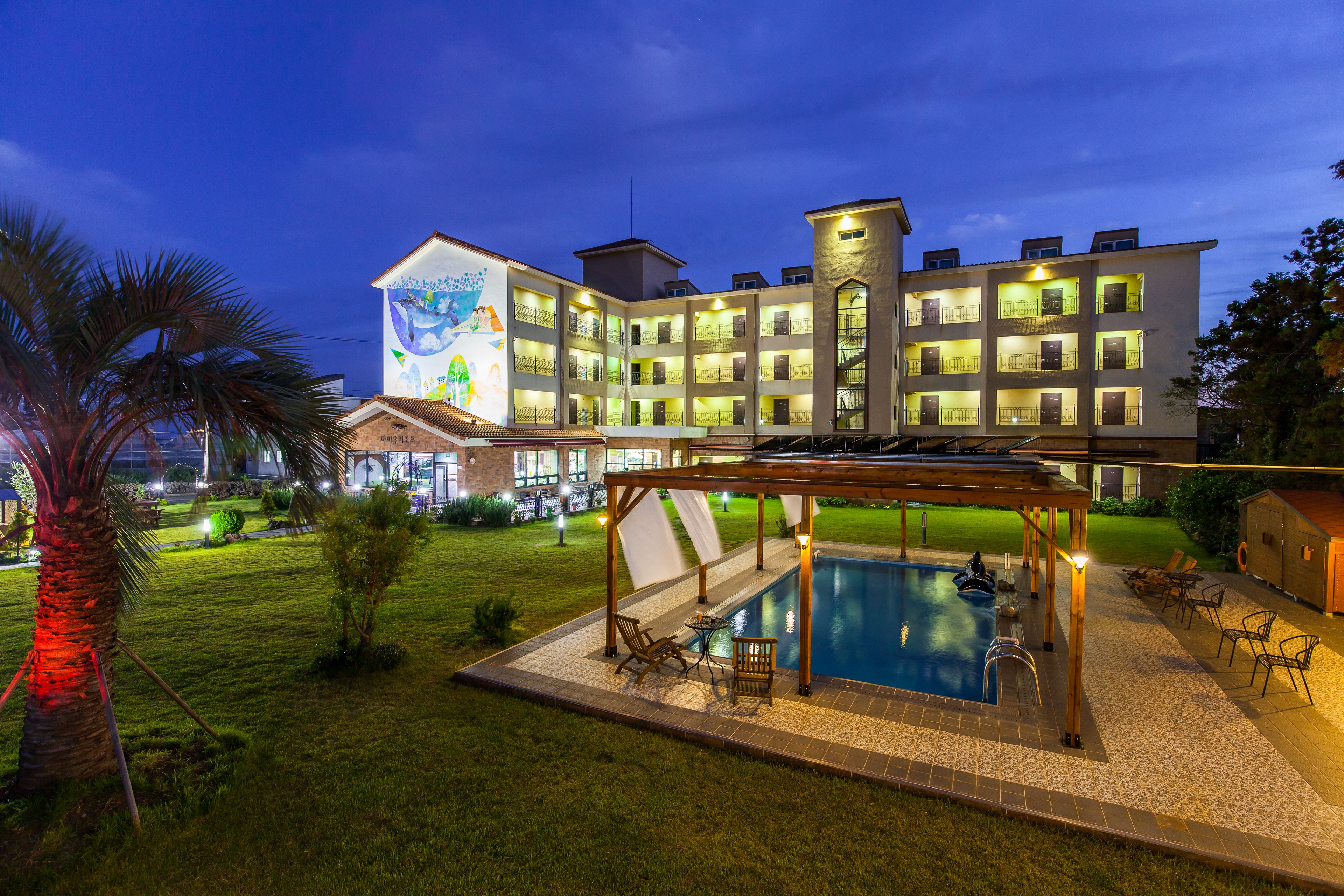 A hotel with a swimming pool, outdoor seating, and a well-lit facade.