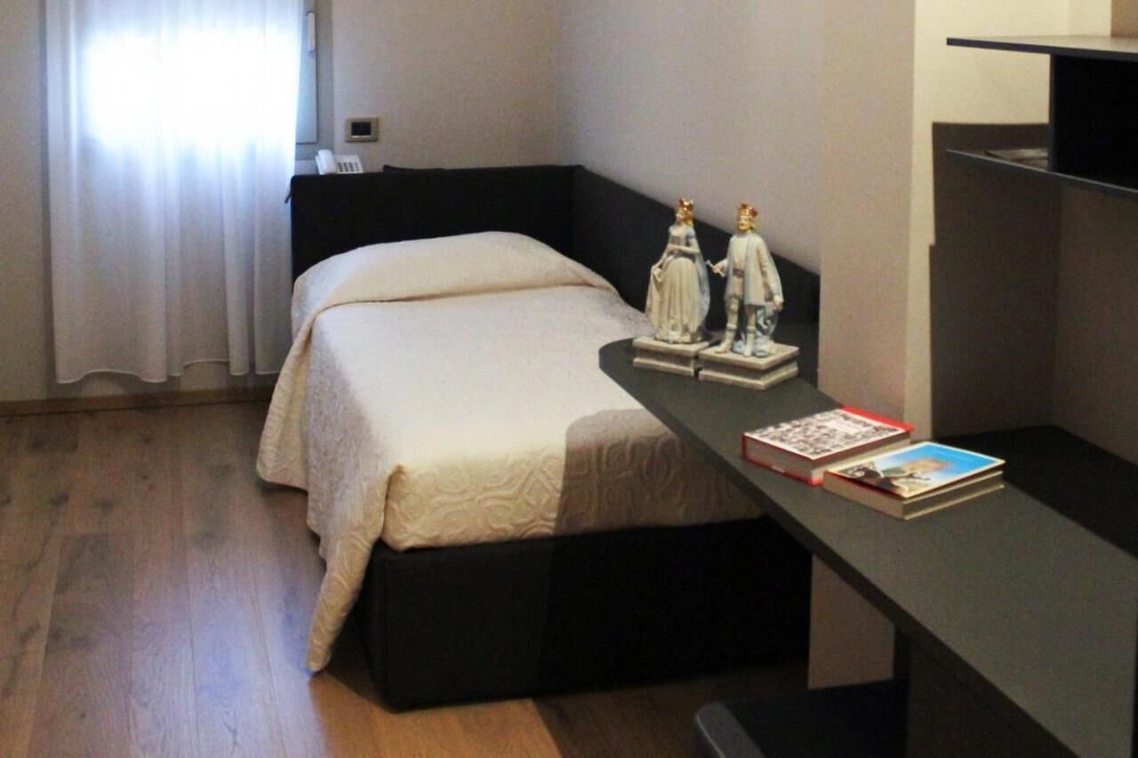 A bedroom with a bed, a nightstand with books, and a statue of a couple.