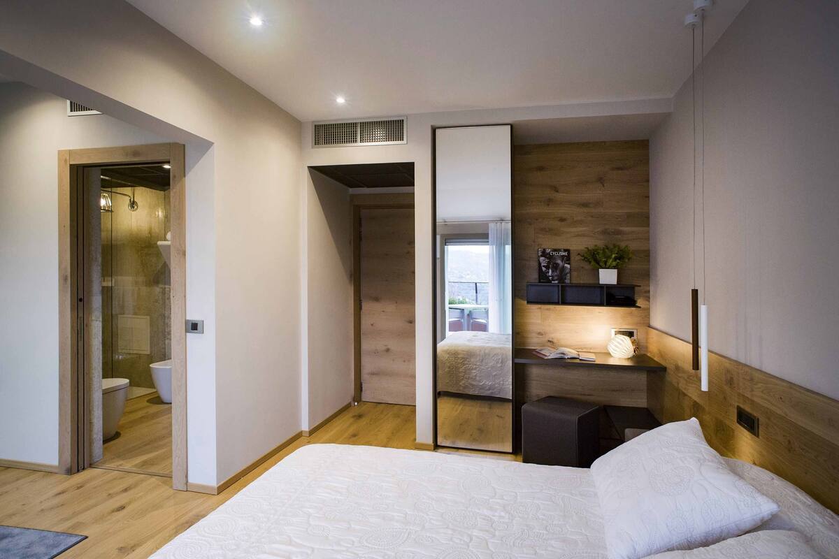 A modern bedroom with a large bed, a desk, and a sliding door leading to a bathroom.