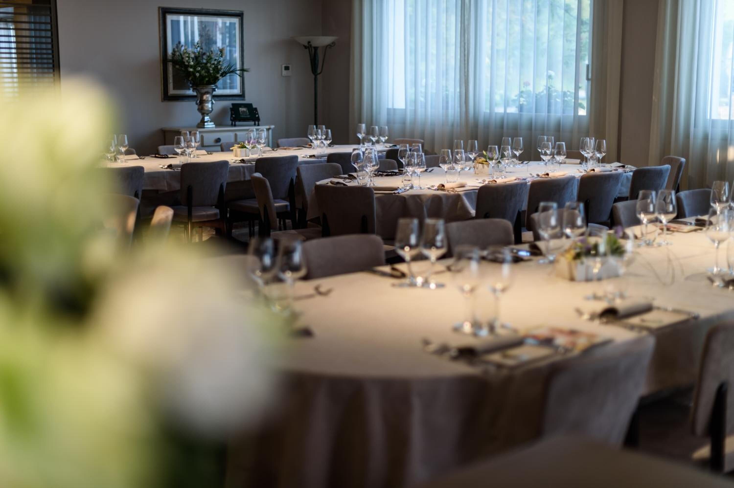 A dining area with multiple tables set for a meal, featuring chairs, wine glasses, and cutlery.