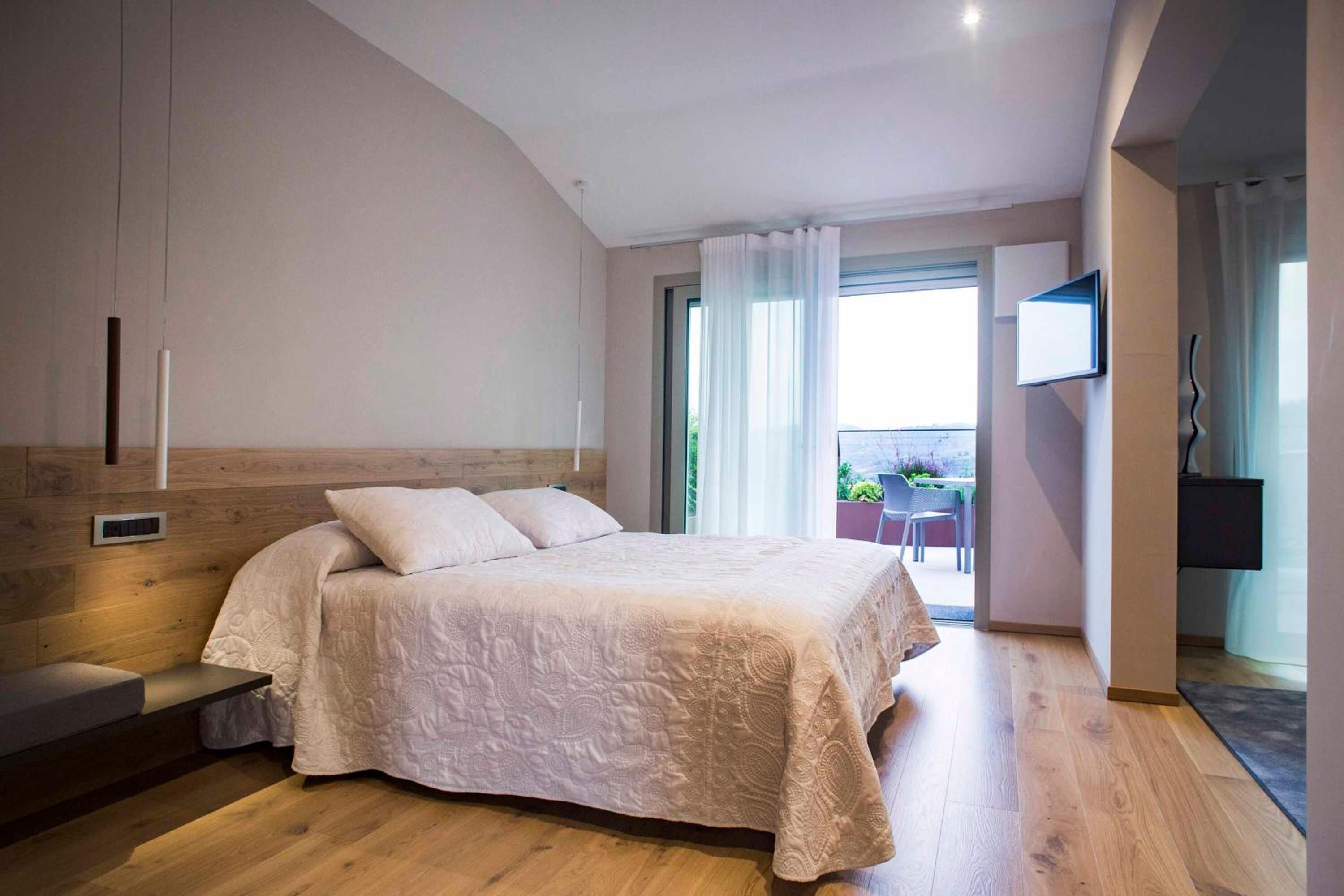Un dormitorio con una cama grande, cabecera de madera, televisión montada en la pared y un balcón con mesa y sillas.