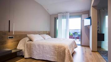 Un dormitorio con una cama grande, cabecera de madera, televisión montada en la pared y un balcón con mesa y sillas.