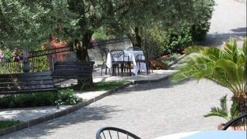 Une cour avec une table et des chaises blanches, entourée de verdure et d’un palmier.