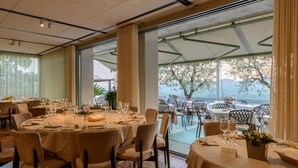 A restaurant with round tables set for dining, large windows offering a view of the outdoors, and a covered outdoor seating area. - Ristorante Hotel La Rosina (Marostica)
