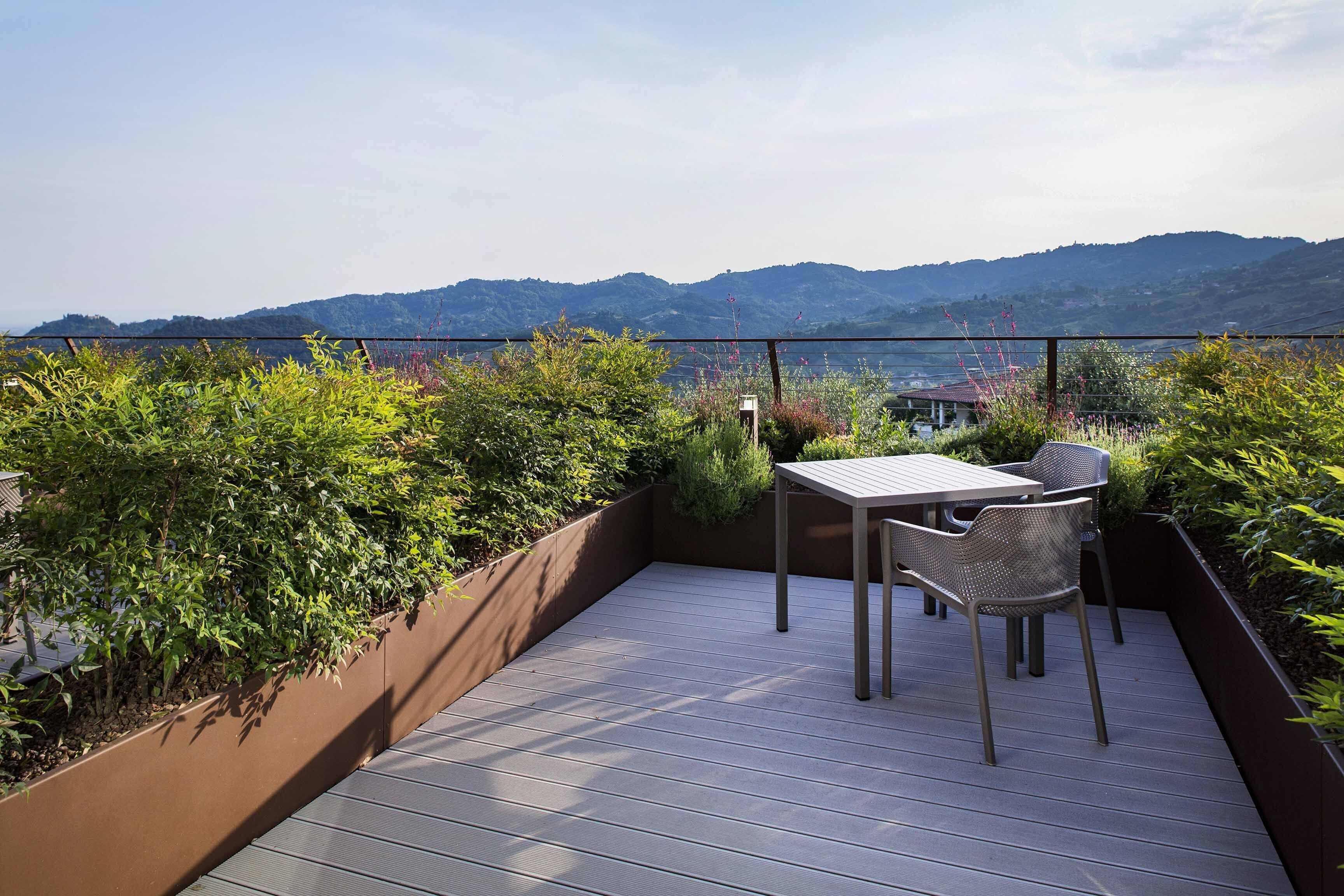Una terraza al aire libre con mesa y sillas, rodeada de exuberante vegetación y con vistas a un paisaje pintoresco.