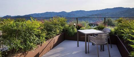 Una terraza al aire libre con mesa y sillas, rodeada de exuberante vegetación y con vistas a un paisaje pintoresco.