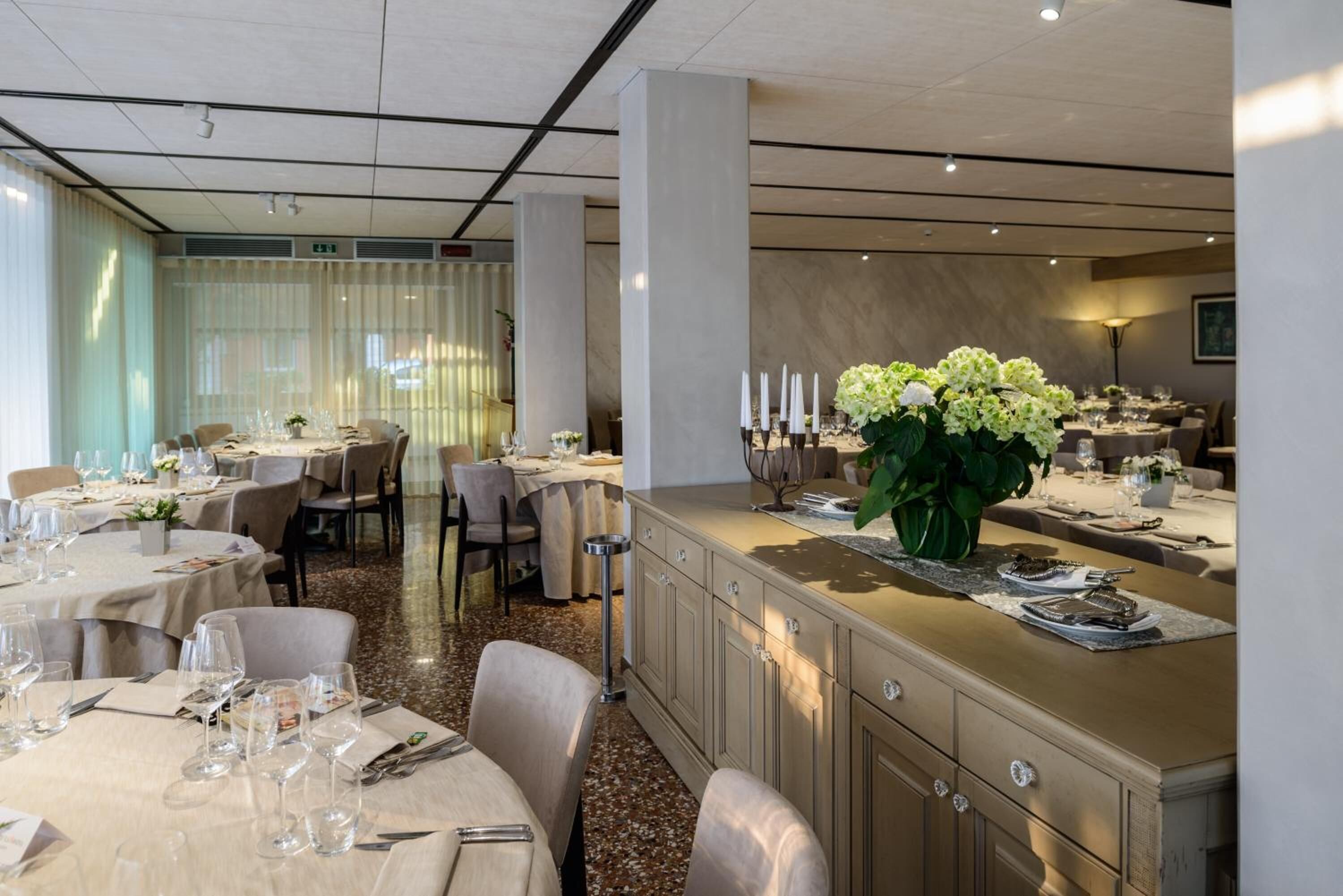 A modern dining area with round tables, chairs, and a central island with a floral arrangement.