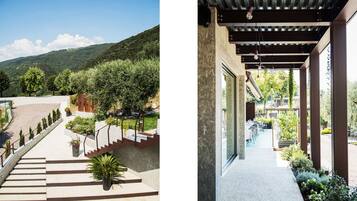 A hotel exterior with a paved outdoor area, steps leading to a covered patio, and a view of a mountainous landscape.