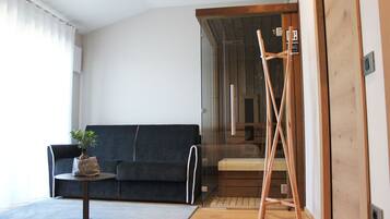 Una sala moderna con un sofá azul oscuro, una mesita redonda con una planta y una escalera de madera apoyada en una puerta de cristal.